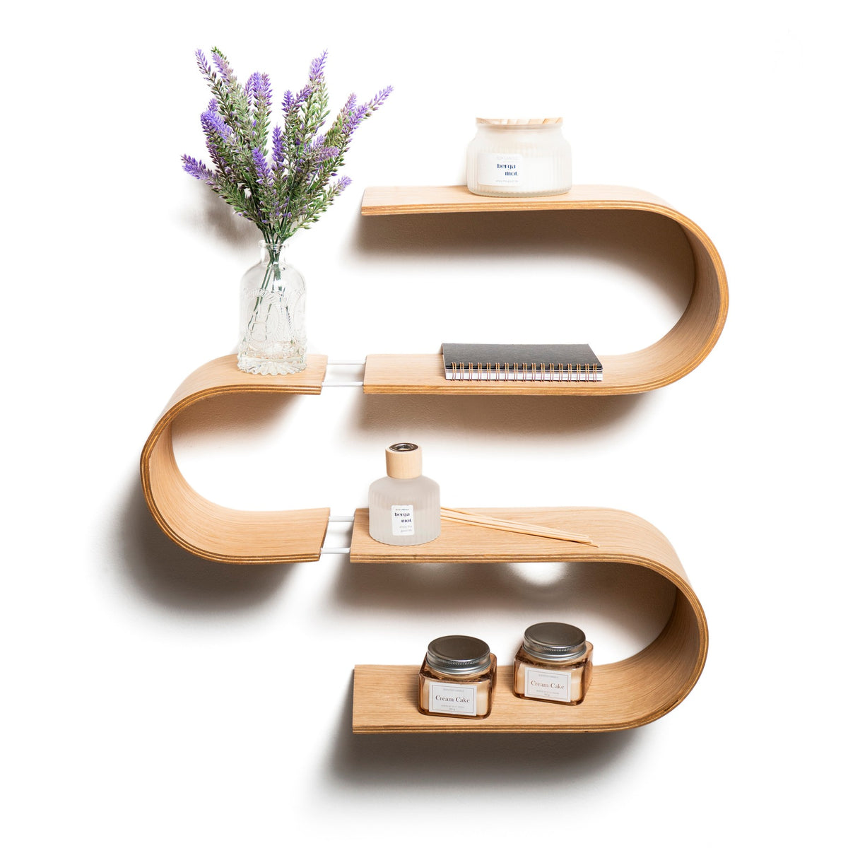 S-shaped wooden floating wall shelf holding lavender, candles and a notebook