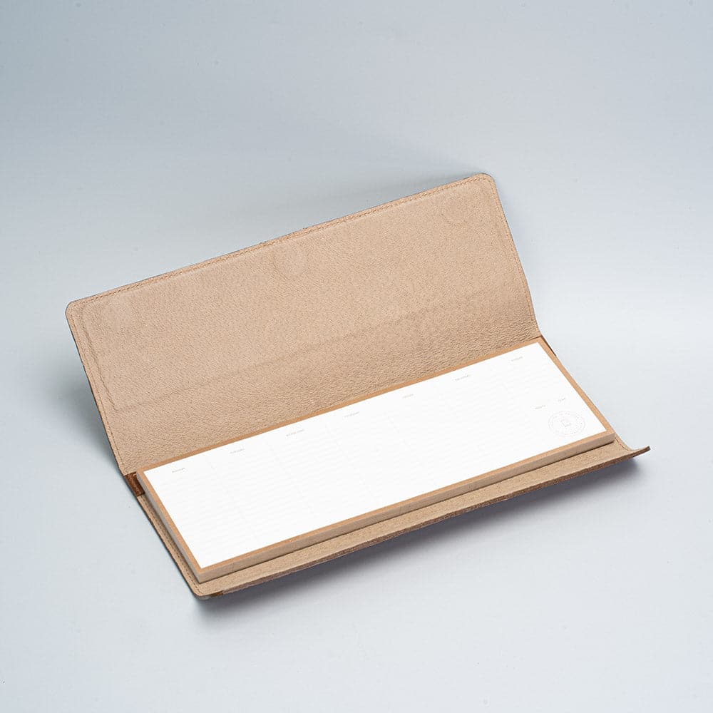 Undated weekly planner pad in a leather holder on a desk